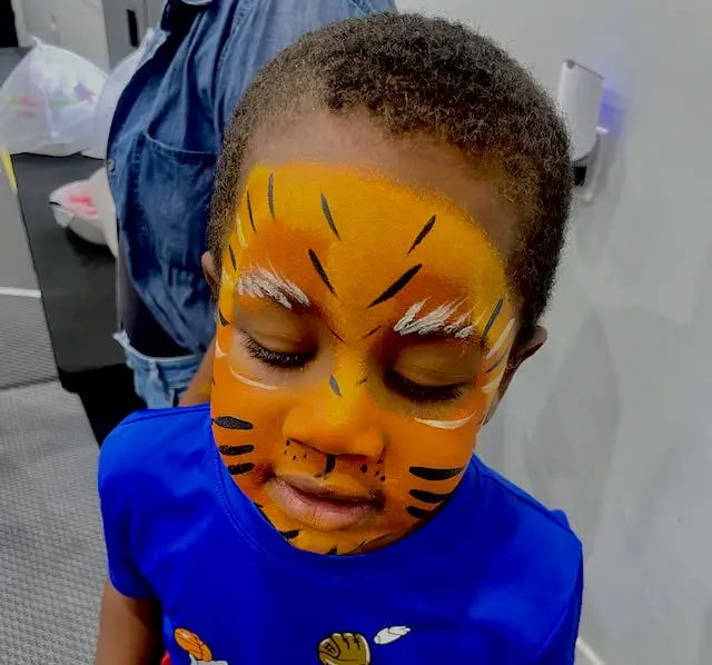 Indianapolis face painter creating a colorful tiger design for a child at a community festival.