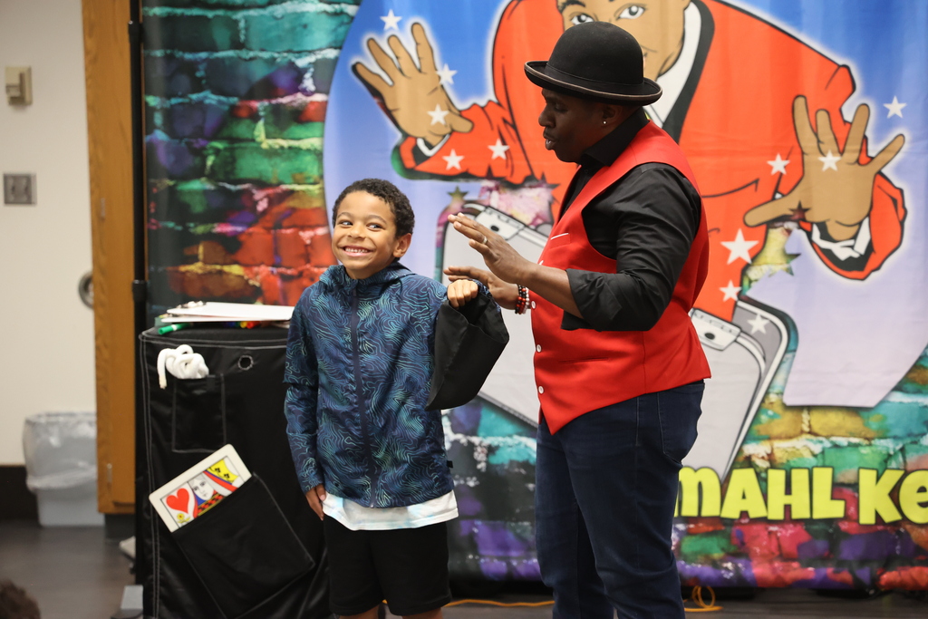 A packed room of Indianapolis families and elementary school students watching a live educational magic show at the Moorhead Community Resource Center during a STEM and Literacy Night event.